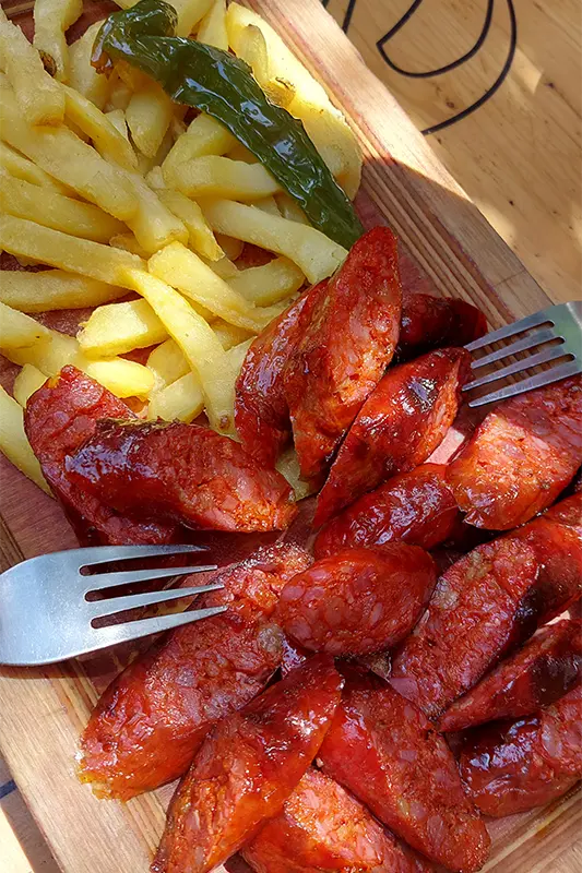 Prato de chorizo grelhado servido com batatas fritas e um pimentão verde