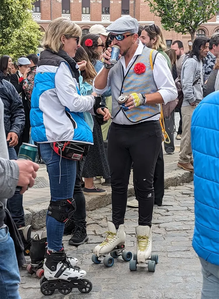 Duas pessoas de patins conversam e bebem na rua durante as festas de San Isidro em Las Vistillas, Madrid.