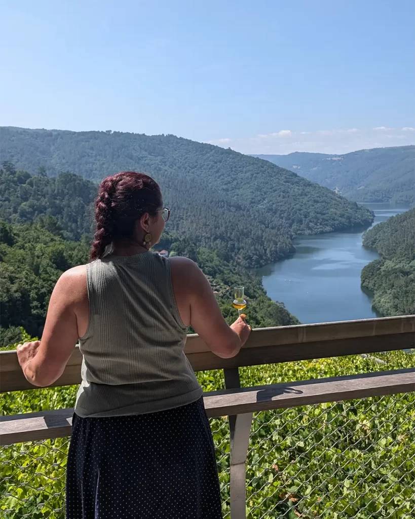 Mulher segurando uma taça de aguardente enquanto aprecia a vista para o rio Sil.