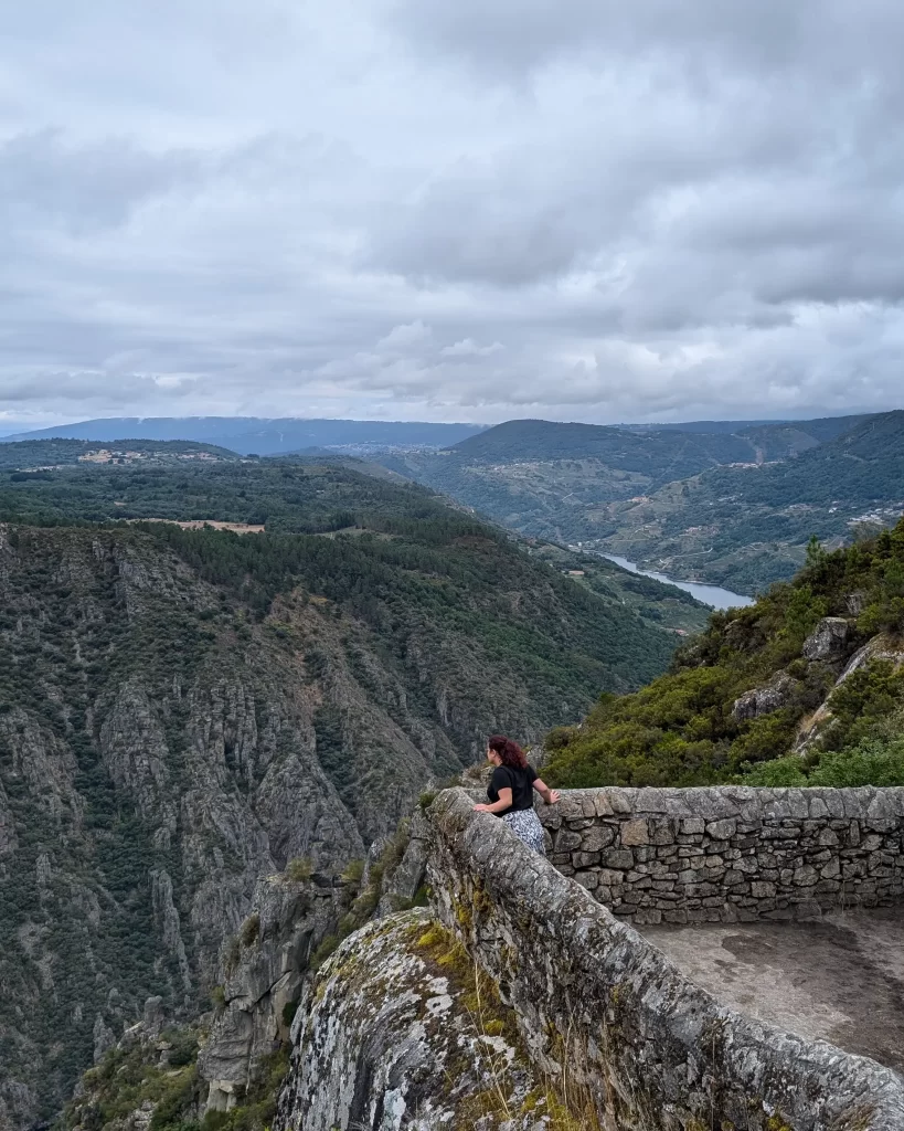 Pessoa contemplando a vista do alto de um mirador de pedra, conhecido como Balcón de Madrid, com montanhas e o Rio Sil ao fundo.