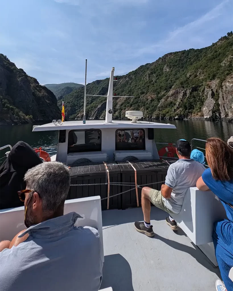 Passageiros no convés de um catamarã navegando pelo Rio Sil, com montanhas ao