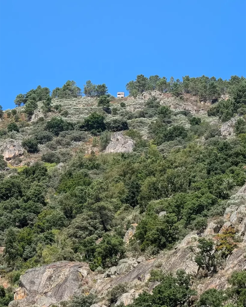 Paisagem montanhosa com vegetação densa e mirador no alto do morro, vista durante o passeio de catamarã no Rio Sil.