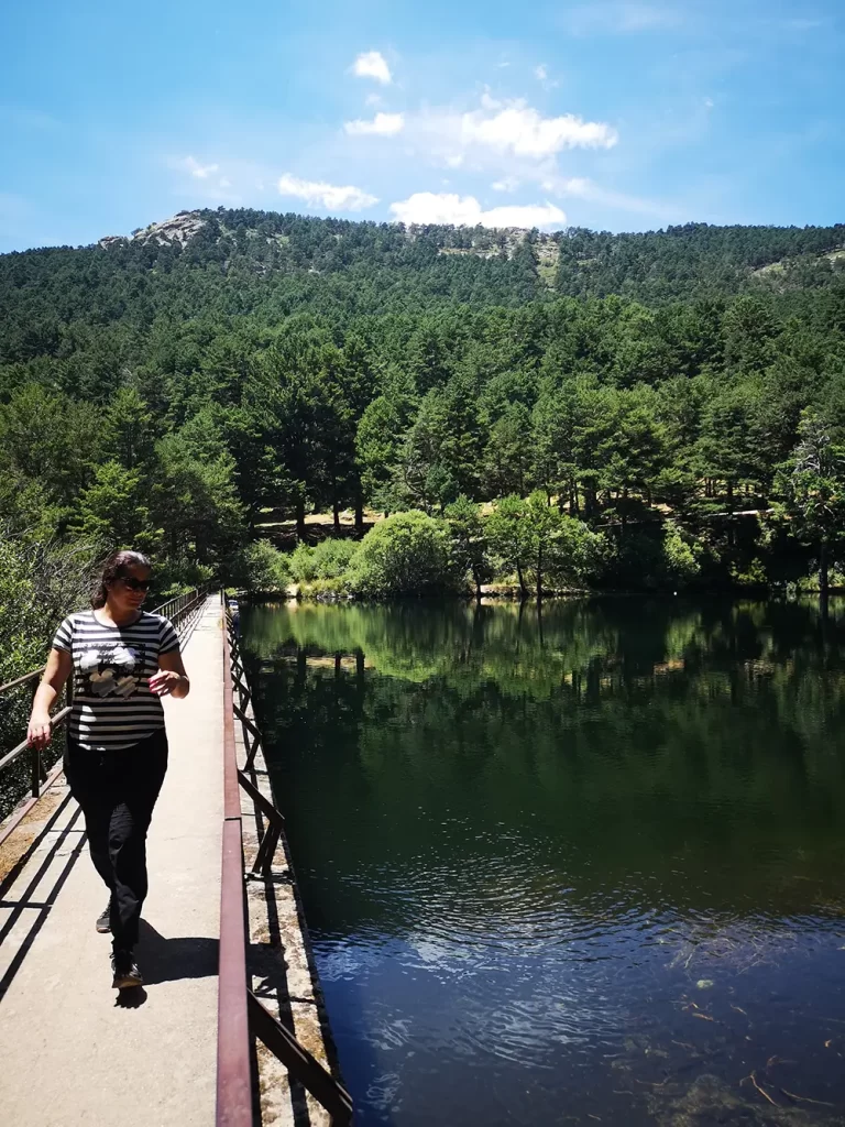 Caminhando em represa sobre um lago rodeado por árvores e montanhas ao fundo, em um dia ensolarado.