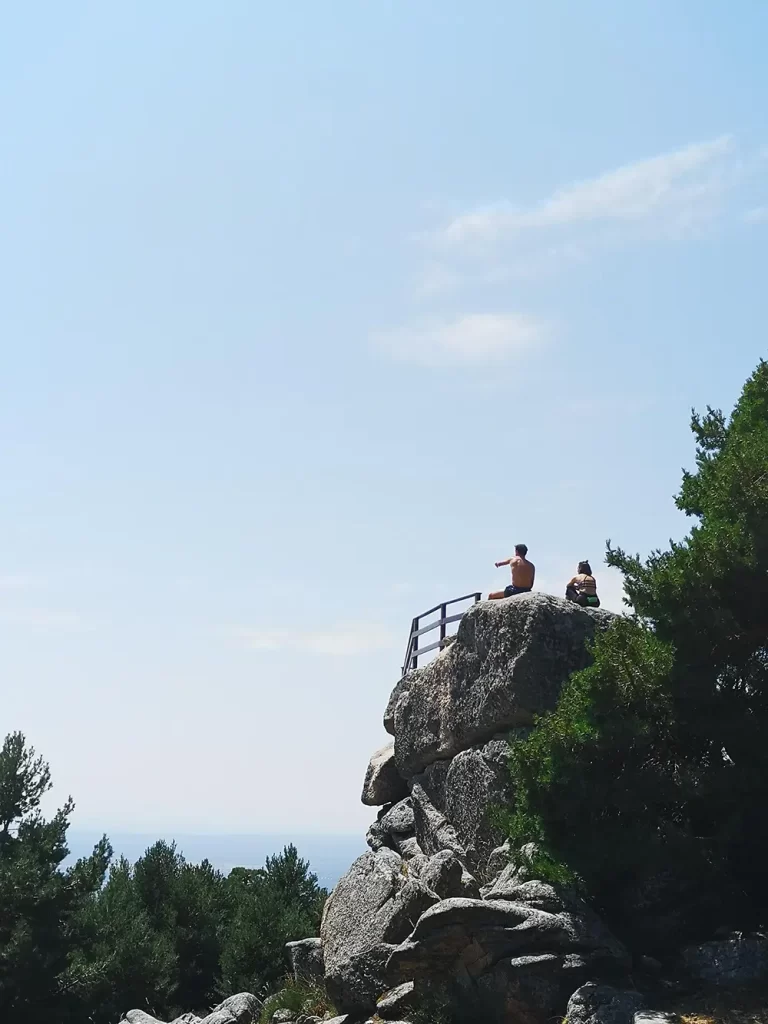 Duas pessoas sentadas em uma grande rocha no Mirador de los Poetas, com vista para as montanhas.