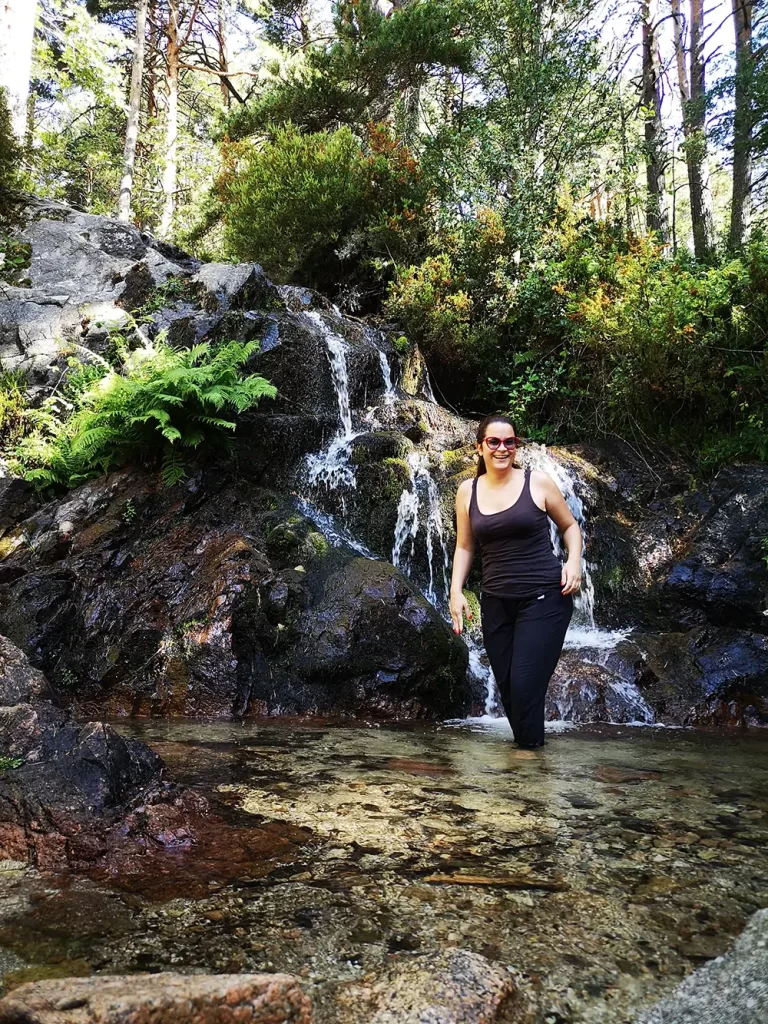 Mulher sorrindo enquanto se refresca em uma pequena cascata na floresta.