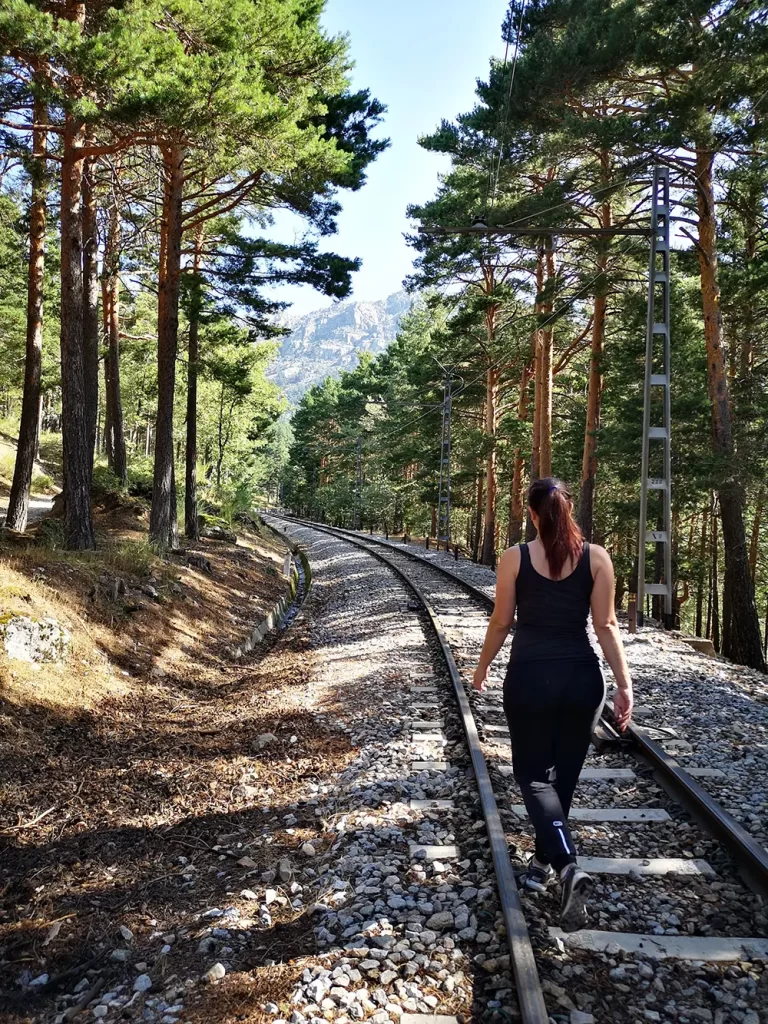 Mulher caminhando ao longo dos trilhos do trem cercados por árvores na Serra de Guadarrama.