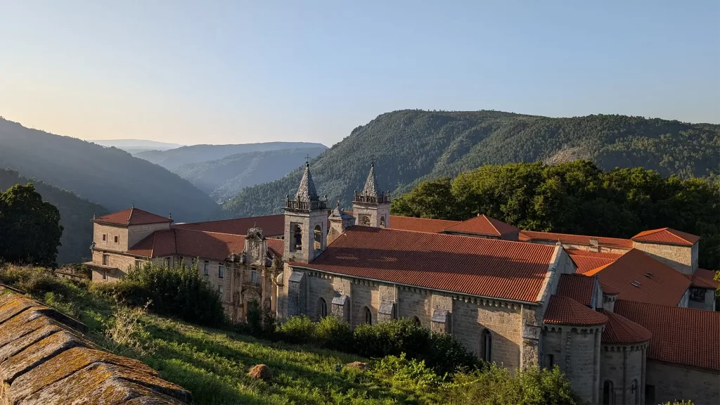 Vista do Parador localizado em um vale cercado por montanhas, destacando a arquitetura histórica do edifício com seus telhados vermelhos e torres imponentes.