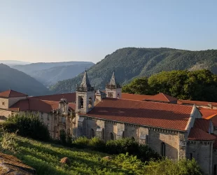 Vista do Parador localizado em um vale cercado por montanhas, destacando a arquitetura histórica do edifício com seus telhados vermelhos e torres imponentes.