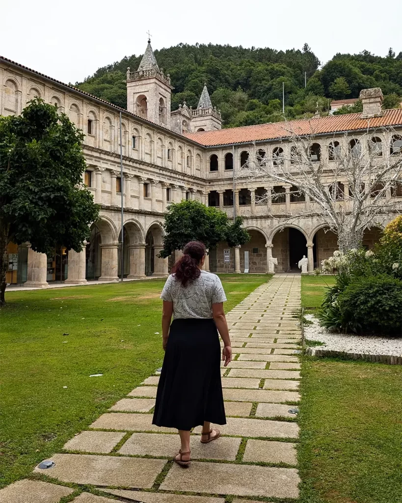 Pessoa caminhando pelo claustro do Monasterio de Santo Estevo de Ribas de Sil, rodeada por arcos e jardins bem cuidados.