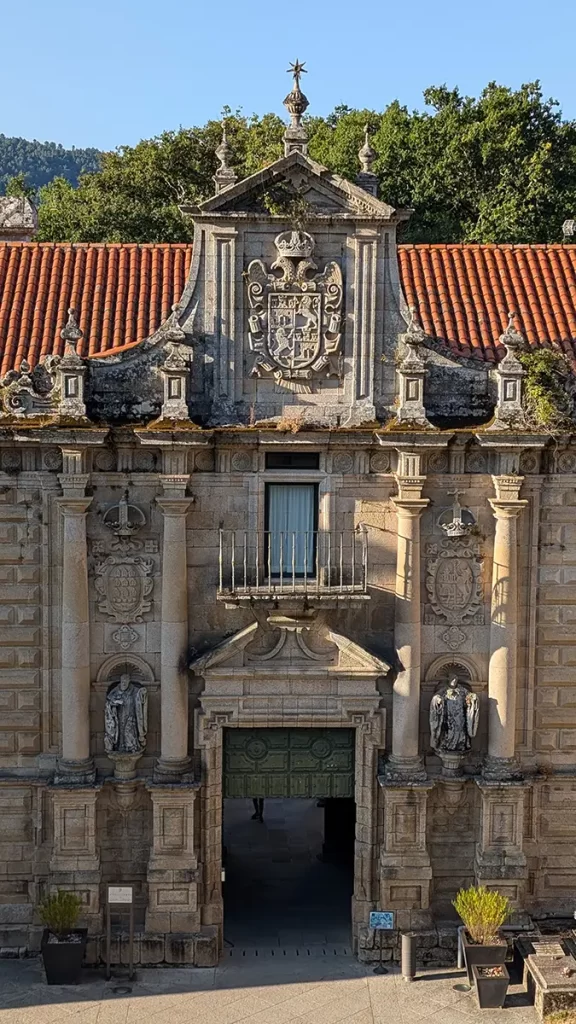 Fachada do Monasterio de Santo Estevo de Ribas de Sil, com detalhes arquitetônicos históricos e o brasão esculpido em pedra.