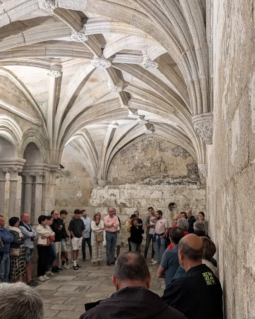 Grupo de pessoas assistindo a uma encenação de um monge durante a visita teatralizada em um salão de pedra do Monasterio de Santo Estevo.