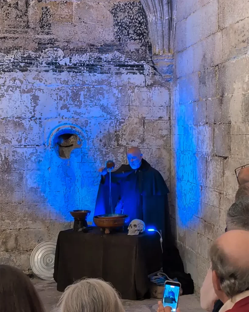 Ator vestido de monge realizando o ritual da Queimada Galega durante a visita teatralizada no Monasterio de Santo Estevo, com iluminação azul e ambiente histórico.