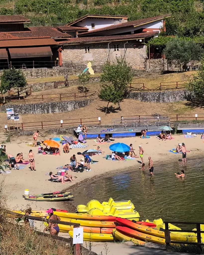 Vista panorâmica da Praia Fluvial de A Cova, com pessoas na areia e barcos de pedais coloridos na beira do rio.