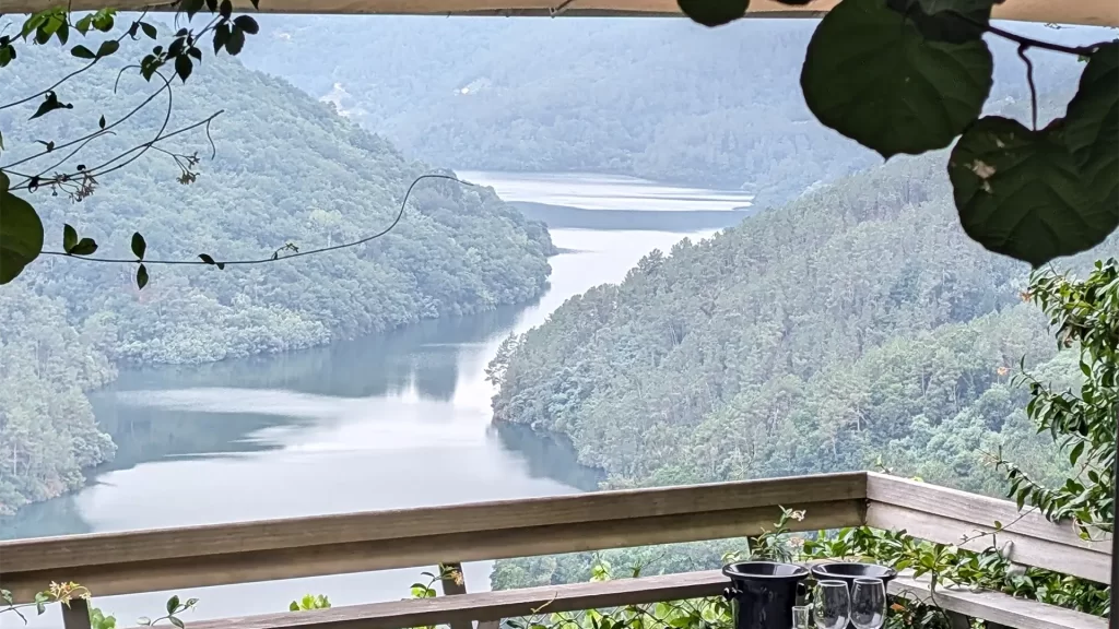 Vista do Rio Sil cercado por montanhas verdes, com folhas e galhos emoldurando a cena na parte superior da imagem.