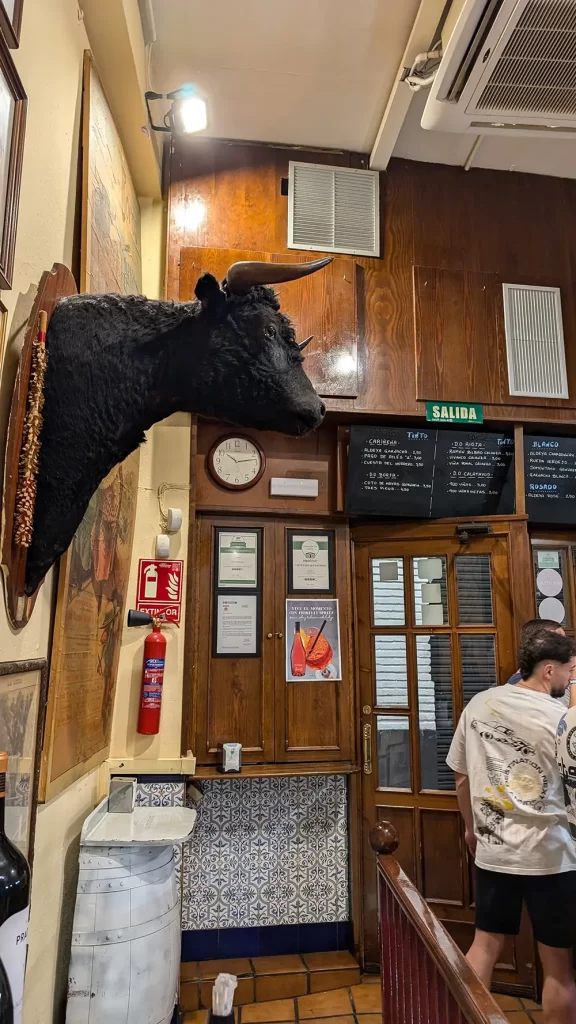 Interior do Bar Victorinos em Zaragoza, mostrando a cabeça de um touro montada na parede, decoração típica de um bar taurino, com cardápio e elementos tradicionais ao fundo.