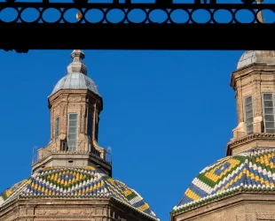 Detalhe das cúpulas da Basílica del Pilar em Zaragoza, Espanha, com telhas coloridas em padrões geométricos, destacando a arquitetura barroca sob um céu azul claro.