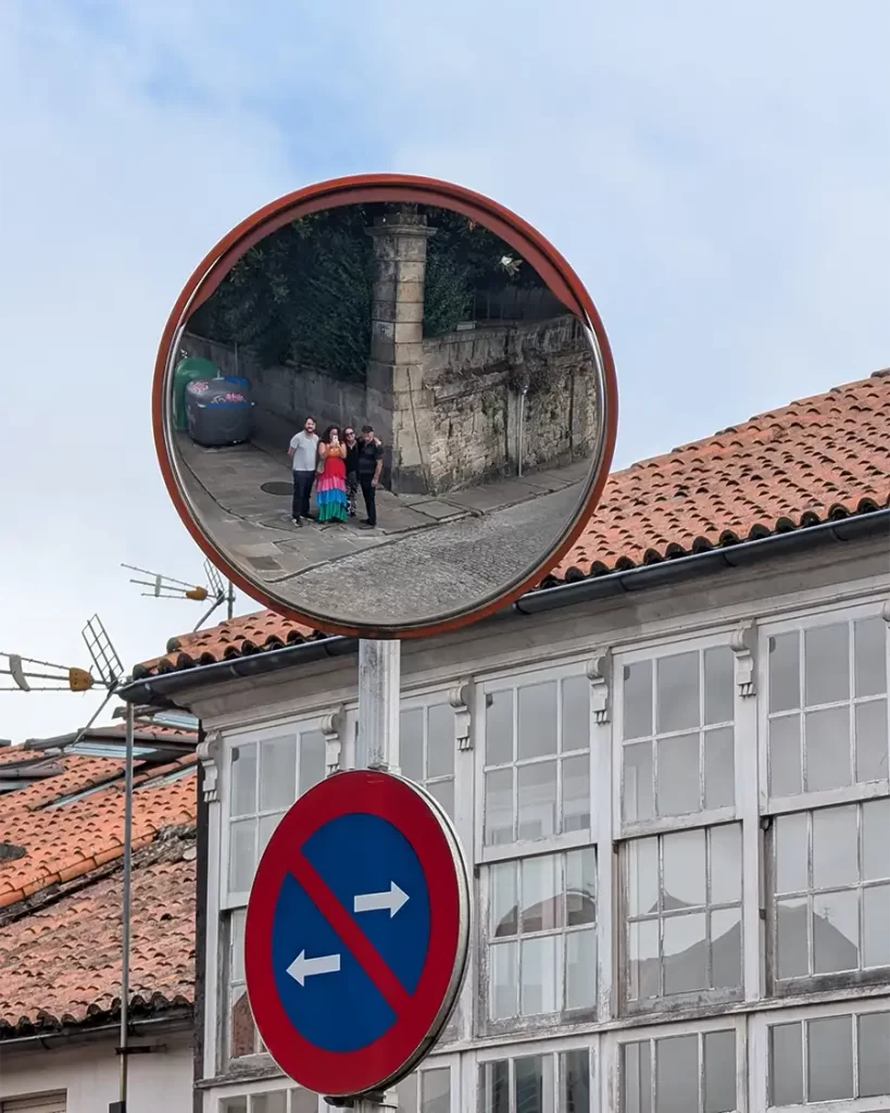 Reflexo de um grupo de turistas em um espelho de trânsito no centro histórico de Santiago de Compostela, com fachadas de casas ao fundo.