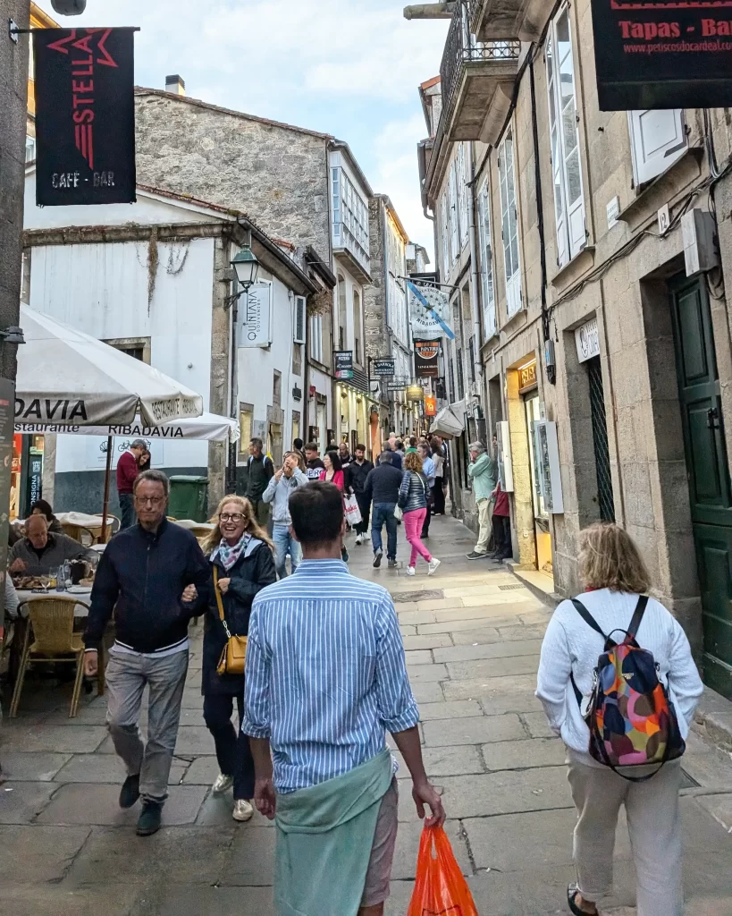 Movimentada rua do centro histórico de Santiago de Compostela, com turistas caminhando entre restaurantes e bares tradicionais.