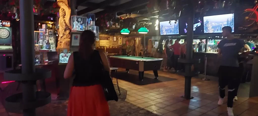 Área interna do Pub Momo com mesa de bilhar e televisões na parede, criando um ambiente descontraído para os frequentadores.