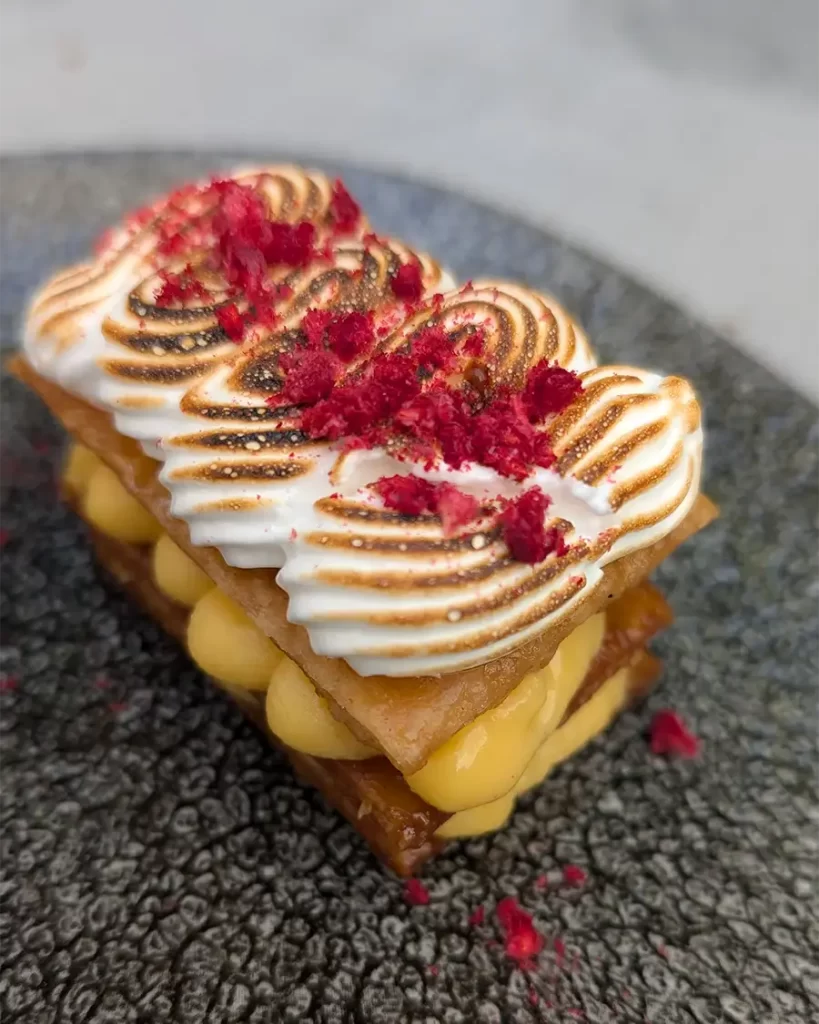 Torta de limão servida no Restaurante Sendeiro, com camadas de massa crocante, creme de limão e merengue flambado, decorada com raspas de frutas vermelhas.