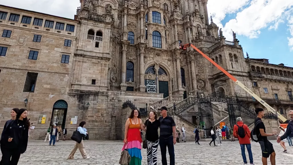 Turistas posam em frente à Catedral de Santiago de Compostela, na Praça do Obradoiro, com a fachada detalhada da catedral ao fundo e movimentação de pedestres ao redor.