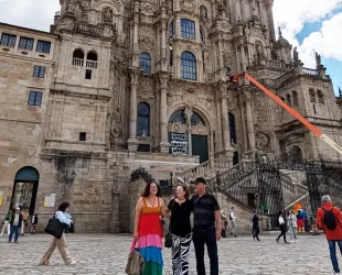 Turistas posam em frente à Catedral de Santiago de Compostela, na Praça do Obradoiro, com a fachada detalhada da catedral ao fundo e movimentação de pedestres ao redor.