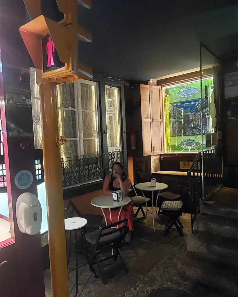 Interior do Pub Momo em Santiago, com mesas e cadeiras próximas a uma janela com vitral colorido e um semáforo decorativo no ambiente.