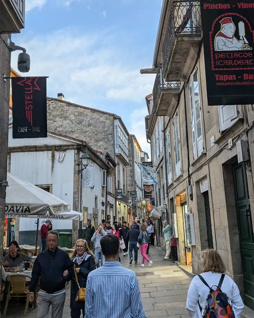 Rua movimentada de Santiago de Compostela, com bares e restaurantes nas laterais, repleta de pessoas caminhando e apreciando o ambiente local