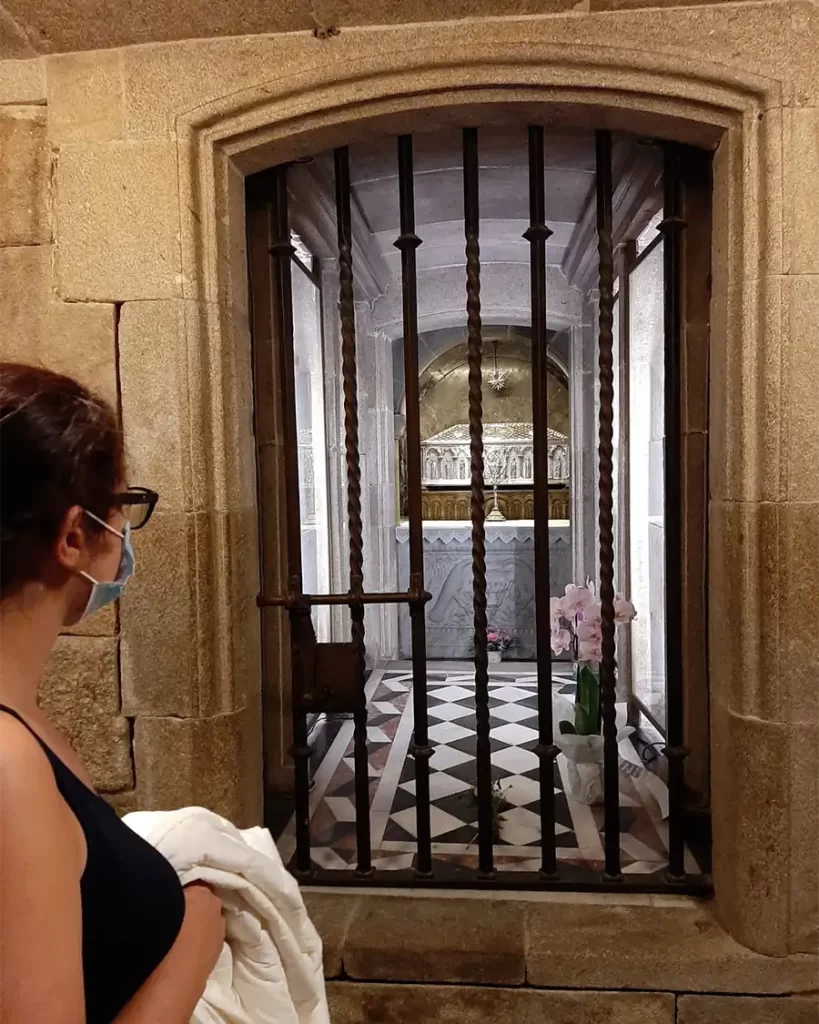 Visitante olhando para o túmulo do Apóstolo Santiago, protegido por grades de metal, na cripta sob o altar principal da Catedral de Santiago de Compostela.