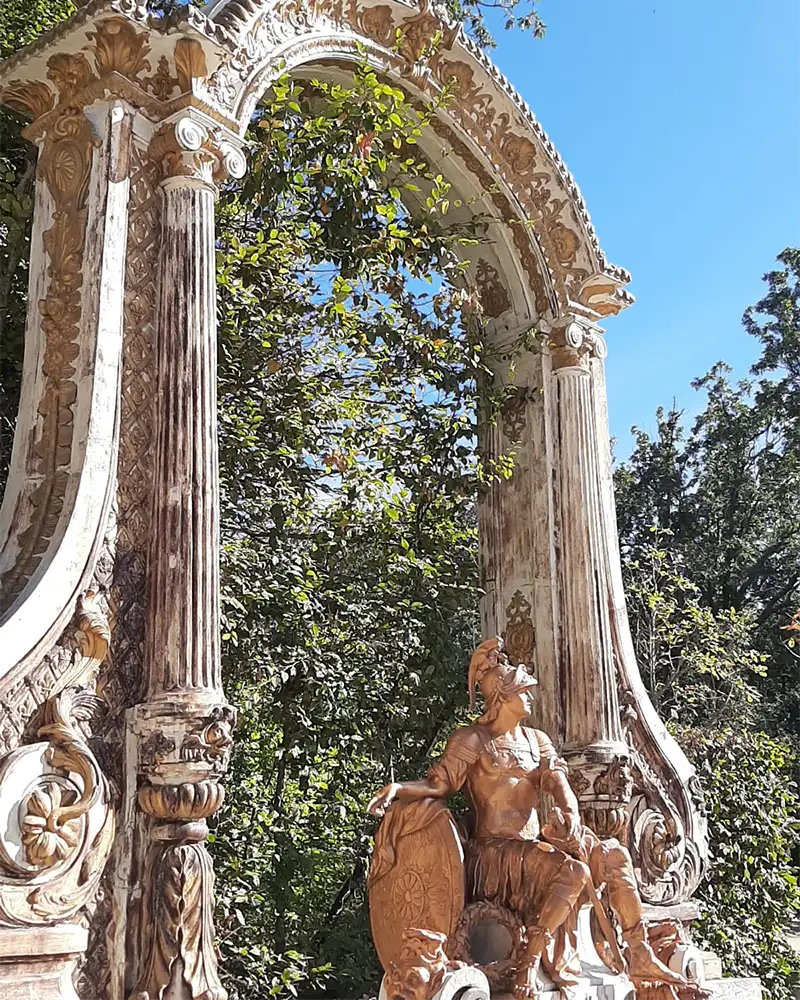 Detalhe de um arco decorado com colunas e uma estátua de figura mitológica em mármore nos jardins de La Granja.