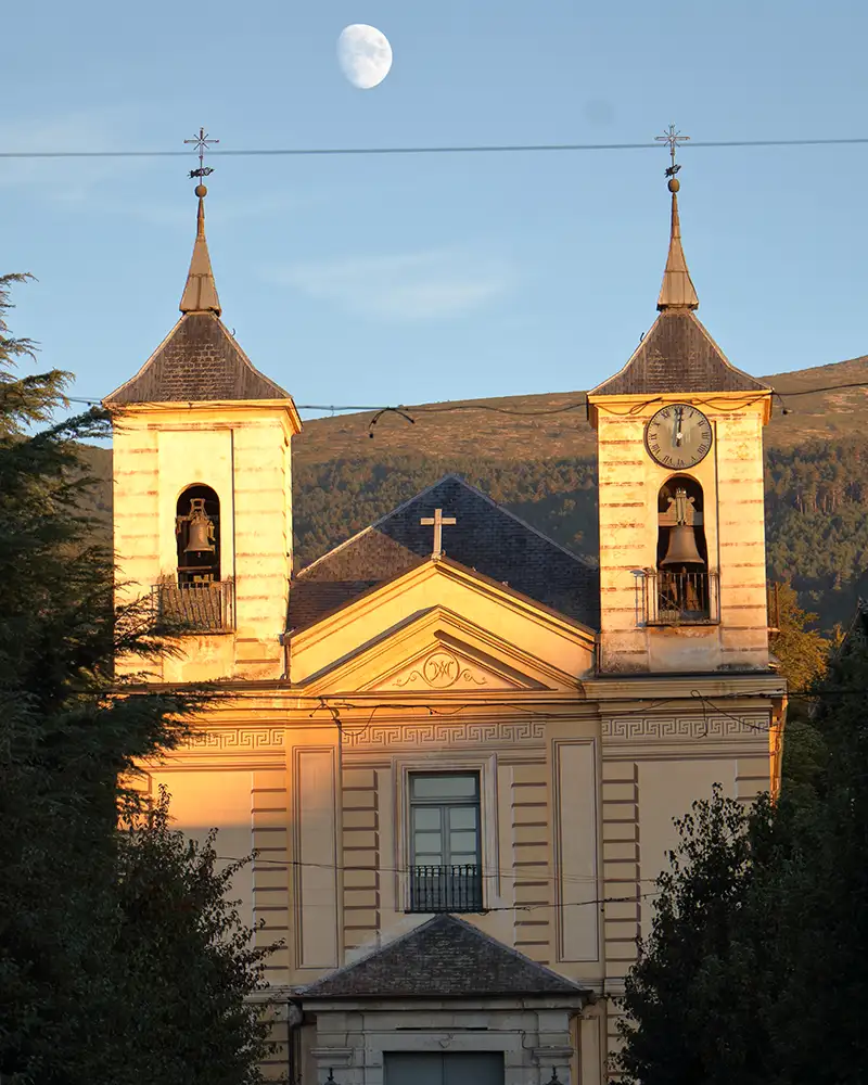 Fachada da igreja de San Ildefonso iluminada pela luz dourada do entardecer, com a lua ao fundo.