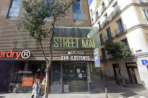Fachada do Mercado de San Ildefonso, localizado na Calle Fuencarral, em Madrid. O letreiro destaca "Street Market," reforçando o conceito de mercado urbano. A entrada de vidro e o design contemporâneo refletem o ambiente moderno e dinâmico do espaço.