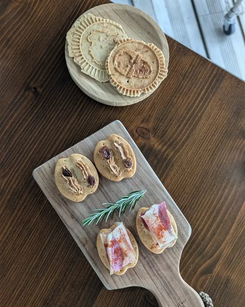 Tábuas de petiscos regionais servidos com bolachas e enfeites de alecrim em uma mesa de madeira.