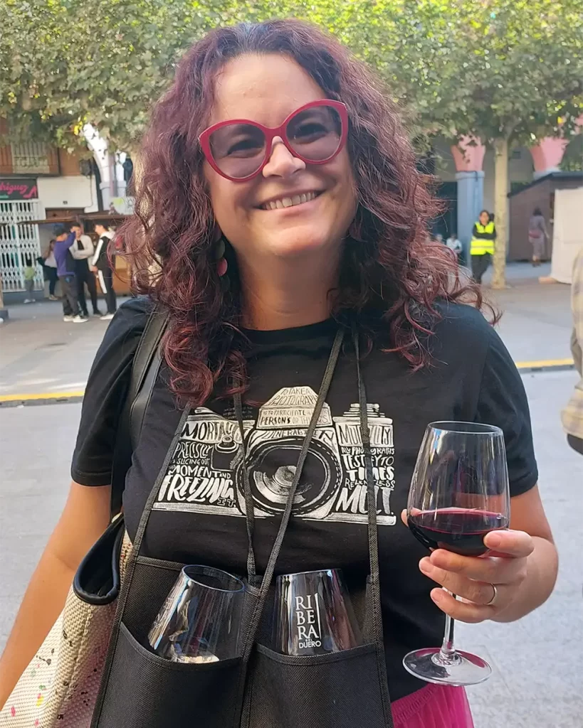 Mulher segurando uma taça de vinho tinto e com duas taças penduradas no pescoço durante a Festa da Vindima em Ribera del Duero.