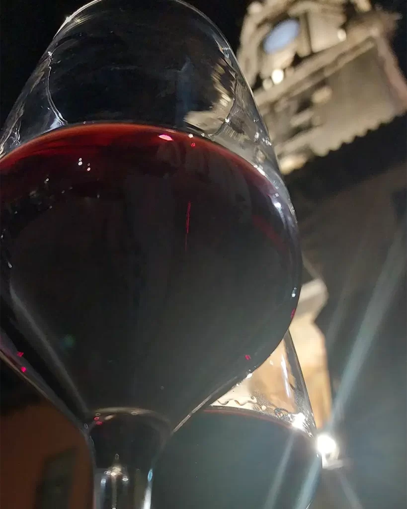 Taça de vinho tinto em primeiro plano com um edifício histórico ao fundo.