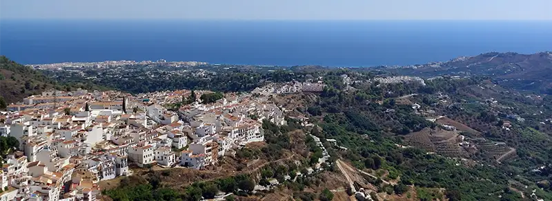 Vista aérea de Frigiliana, um dos Pueblos Blancos da Andaluzia, com suas casas brancas nas colinas e o Mar Mediterrâneo ao fundo.