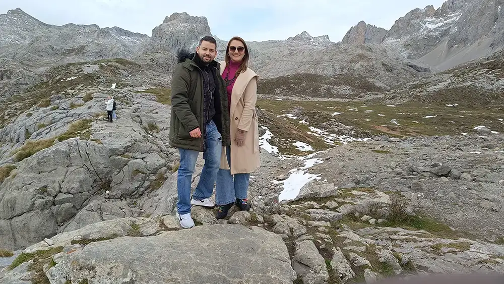 Casal posando entre as montanhas rochosas de Fuente Dé, nos Picos da Europa, com neve ao fundo.