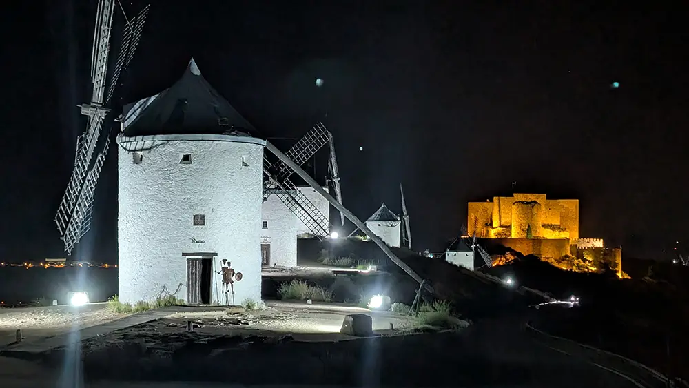 Moinho Rucio e castelo de Consuegra iluminados à noite com destaque para as pás em movimento