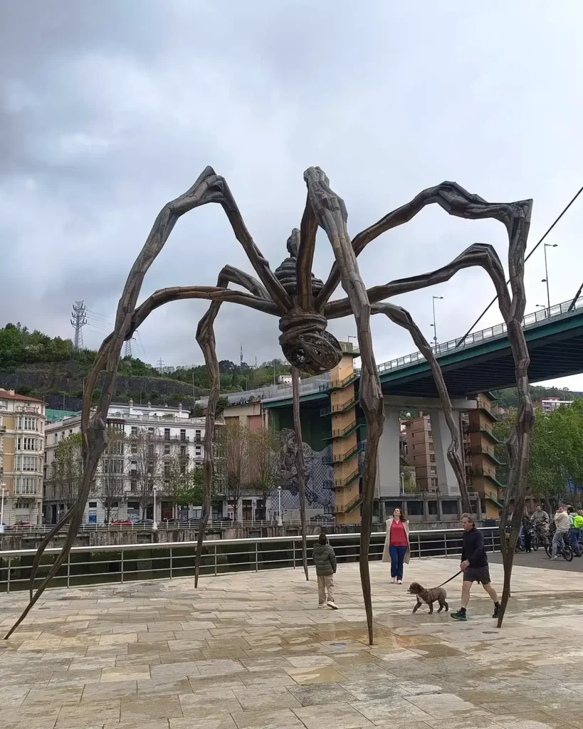 Escultura Maman em frente ao Museu Guggenheim Bilbao, com visitantes circulando sob as pernas da aranha
