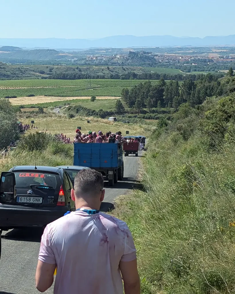 Tractor lleno de participantes vestidos de rosa avanzando por una carretera rural rodeada de viñedos en Haro