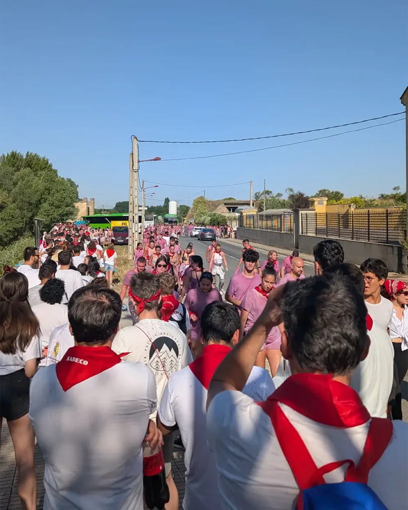 Multidão de participantes da Batalha do Vinho de Haro esperando o ônibus. A maioria veste camisetas brancas, muitas manchadas de roxo, e usam o tradicional lenço vermelho.