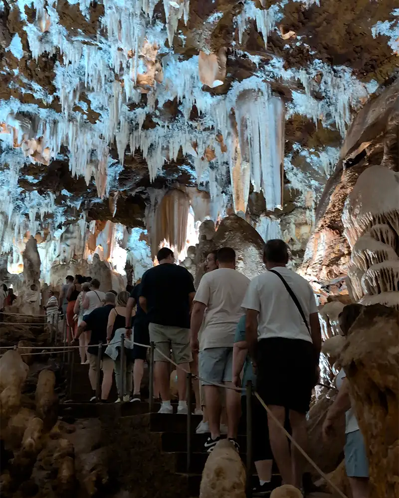 Turistas caminhando em fila por um trecho estreito do percurso da Cueva del Águila, com o teto coberto por estalactites.