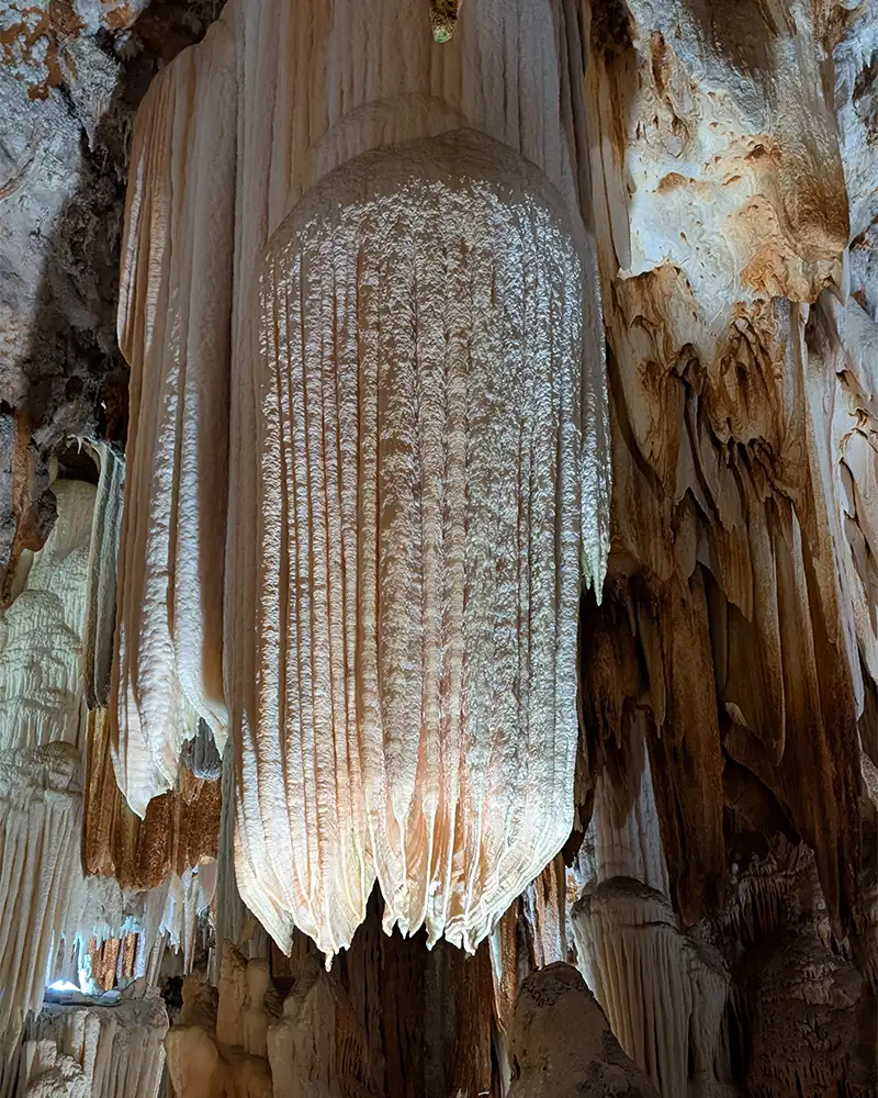 "Close-up de uma grande formação rochosa na Cueva del Águila, com textura que lembra uma cortina de pedra iluminada.