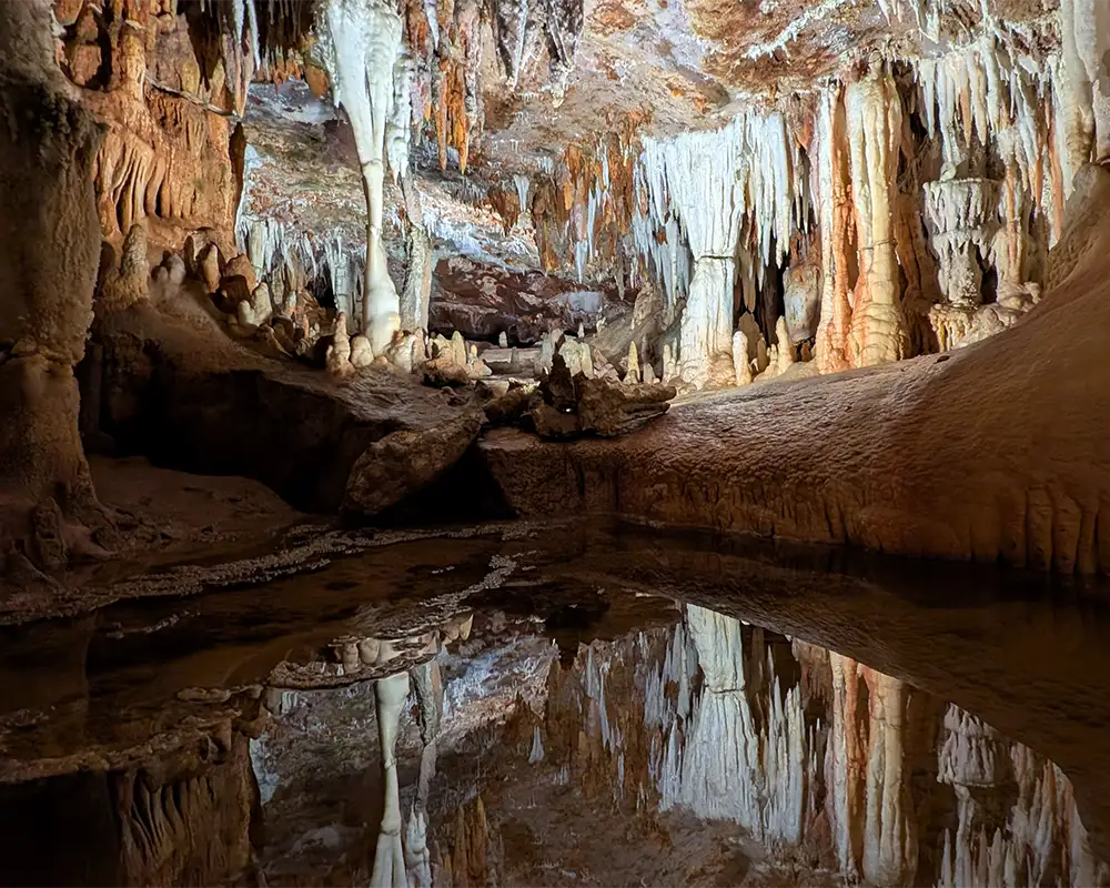 Poça de água no chão da Cueva del Águila criando um reflexo perfeito das estalactites e formações rochosas.