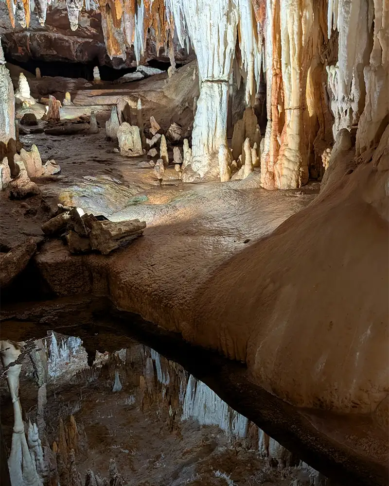 Vista do percurso no chão da Cueva del Águila, mostrando o caminho que passa entre grandes formações rochosas e poças d'água.