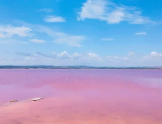 Paisagem da Laguna Rosa de Torrevieja, na Espanha, com a água em tons de rosa calmos refletindo o céu azul com nuvens.