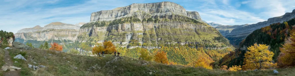 Vista panorâmica do Vale de Ordesa com encostas cobertas de vegetação amarela e altas montanhas rochosas ao fundo.