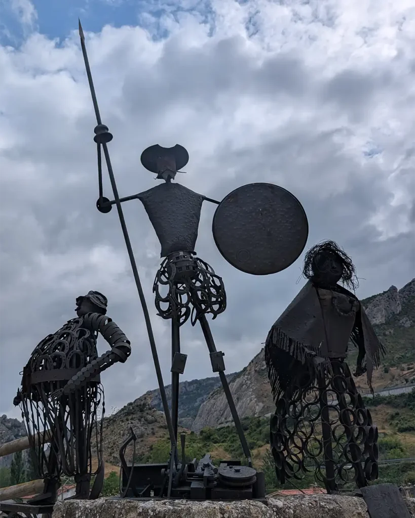 Esculturas de metal de Dom Quixote, Sancho Pança e Dulcinea feitas com peças recicladas, com as montanhas de Pancorbo ao fundo.