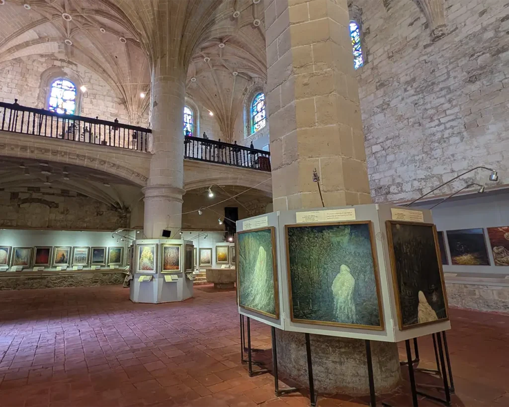 Interior da Igreja de Santiago em Pancorbo, convertida em museu, com uma exposição de arte montada entre os pilares de pedra e o teto abobadado.