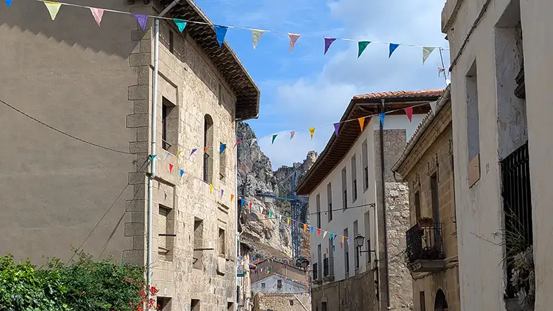 Rua principal do pueblo de Pancorbo, com casas de pedra e bandeirinhas coloridas, e as rochas do desfiladeiro ao fundo.
